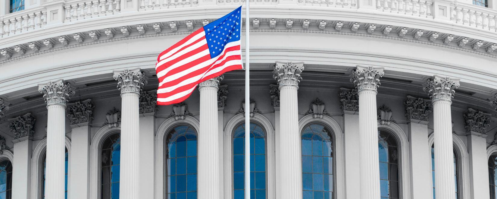 A close-up of the United States Capitol rotunda with the U.S. flag in the foreground. 