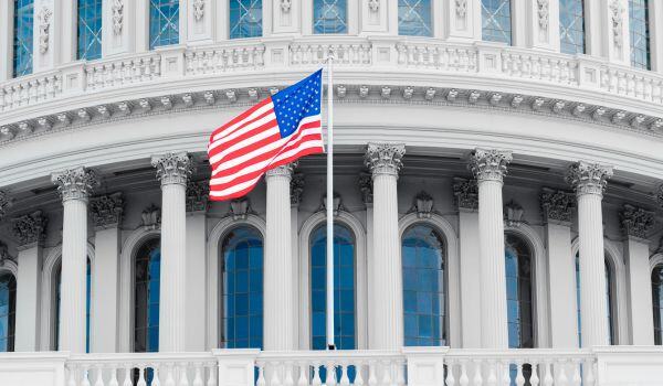 A close-up of the United States Capitol rotunda with the U.S. flag in the foreground.