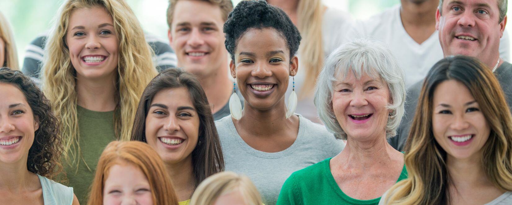 A smiling group of multi-racial, multi-generational people smiling at the camera. 