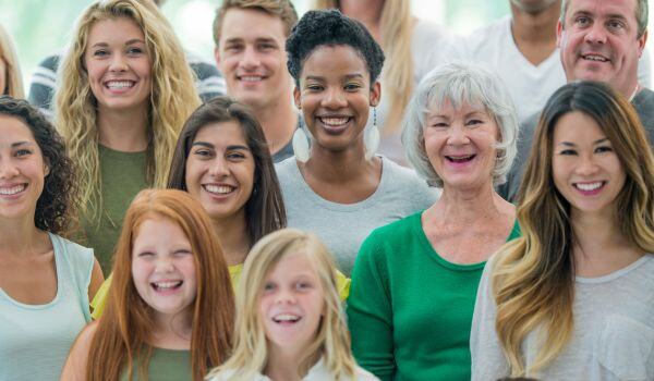 A smiling group of multi-racial, multi-generational people smiling at the camera. 