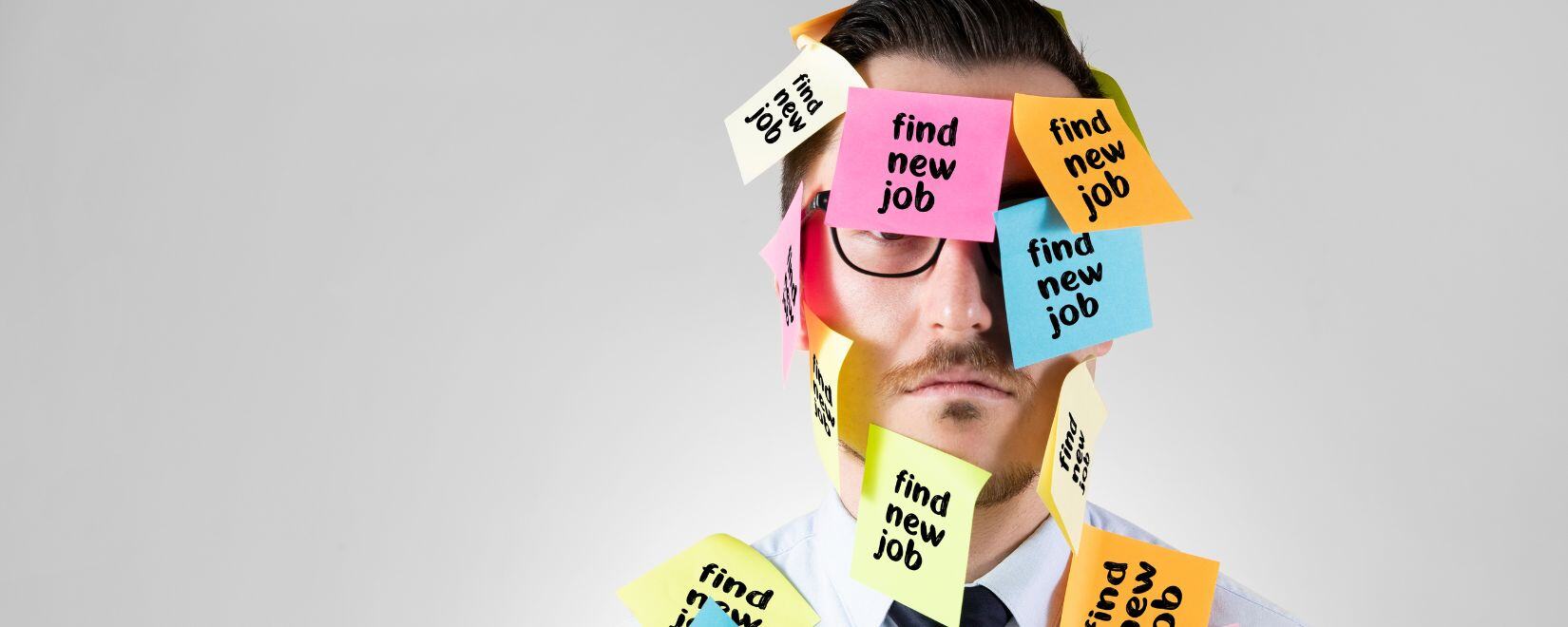 A man with glasses in a shirt and tie with his face covered with post-it notes saying “find new job.”